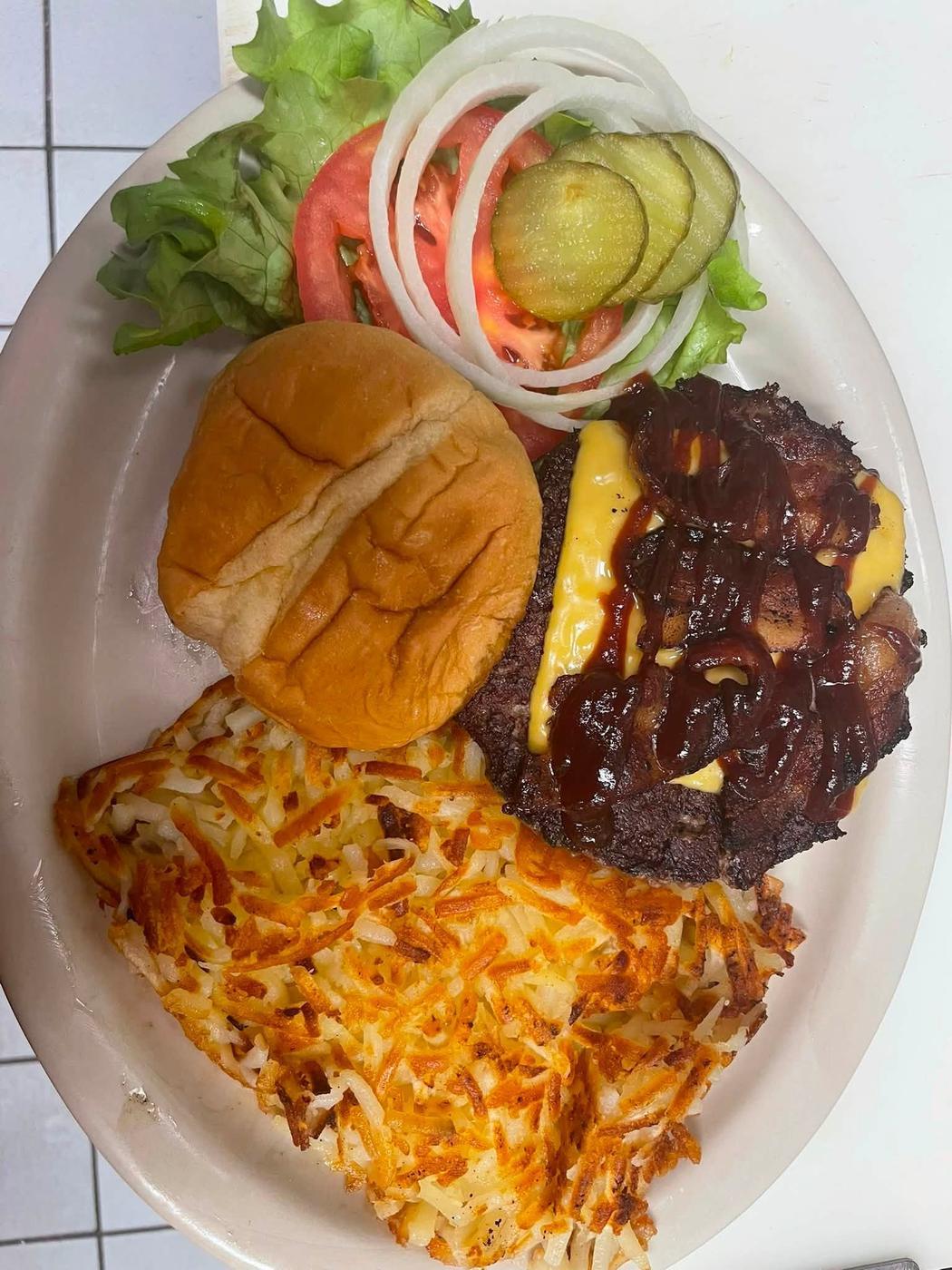 A cheeseburger with bacon and barbecue sauce, bun to the side, with hash browns and salad.