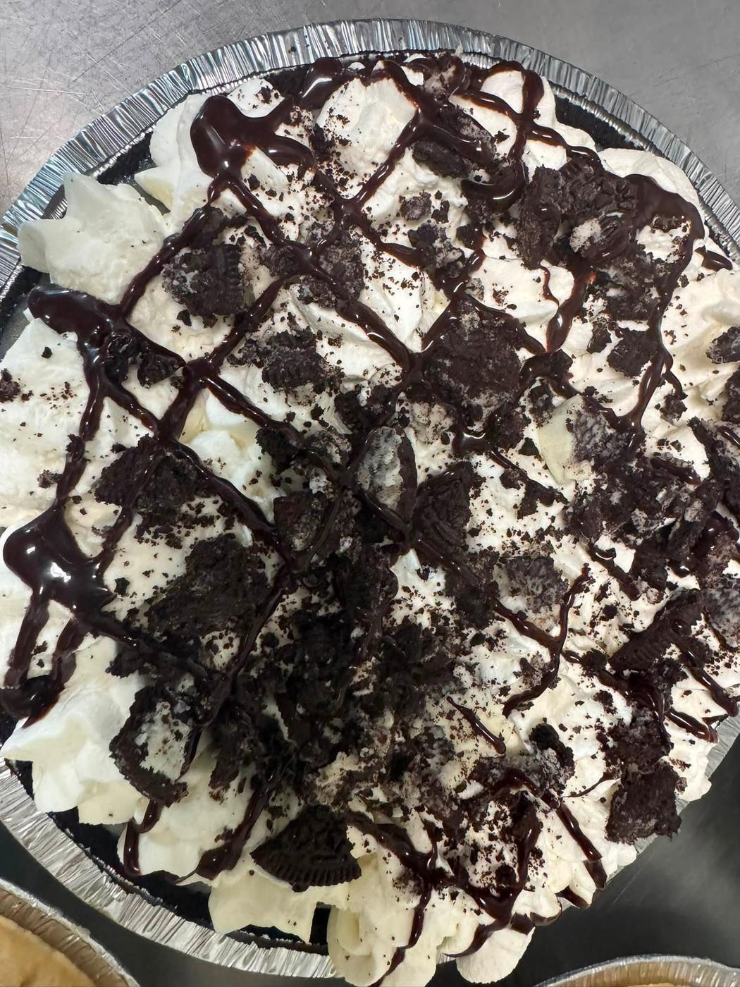 A cookies and cream pie with chocolate drizzled across the whipped cream.