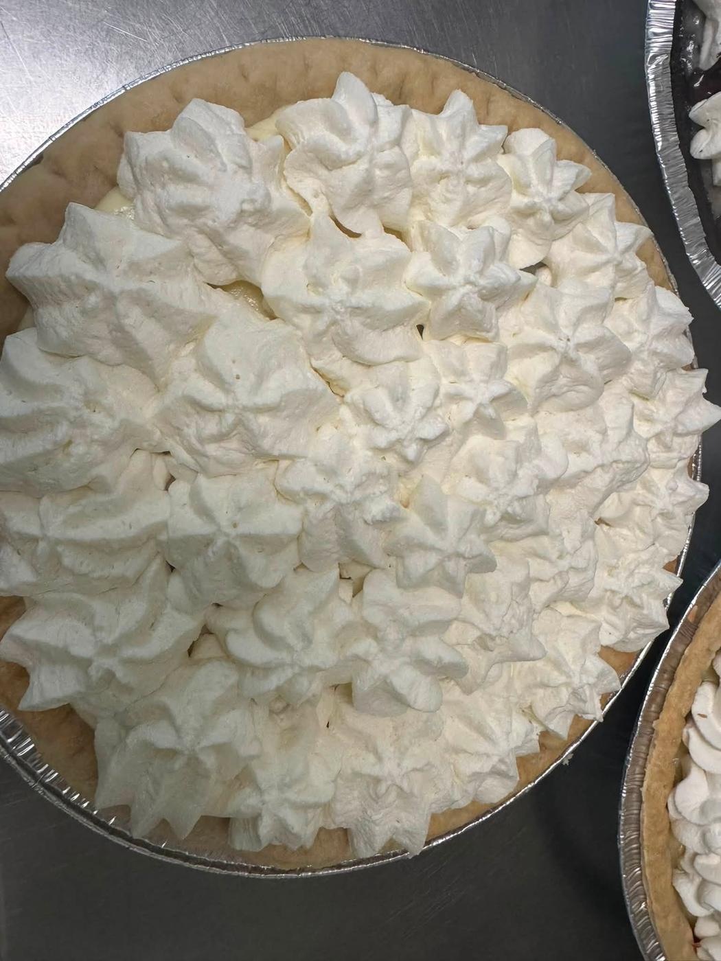 A cream pie topped edge to edge with whipped cream piped by hand.