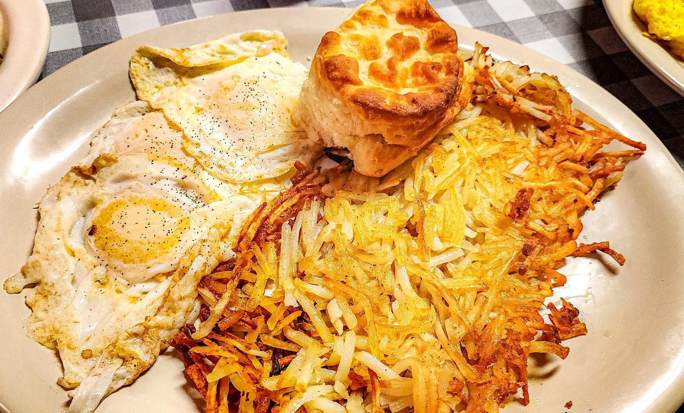 Two fried eggs beside a wide bed of golden hash browns and a tall split biscuit.