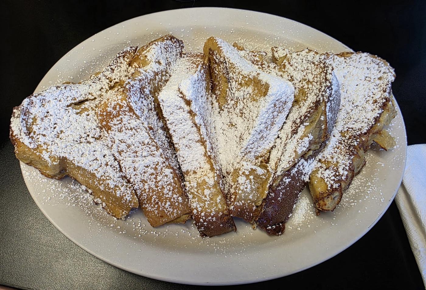 Thick slices of french toast under powdered sugar, filling an oval platter.