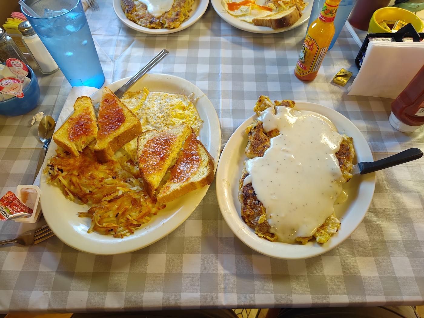 A gingham table laid with jam and toast, hash browns, eggs, and a skillet of chicken fried steak under gravy.